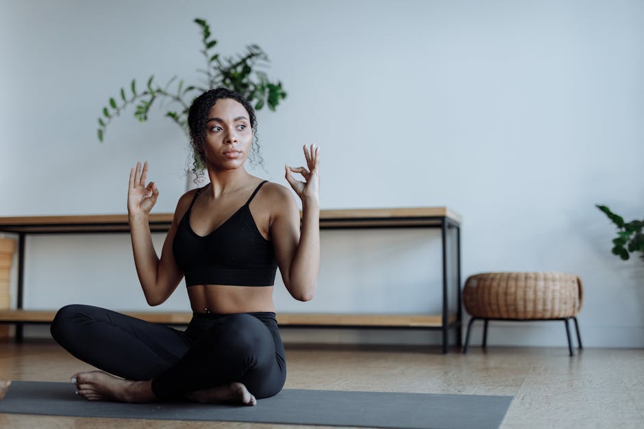 Woman meditating in a lotus pose on a yoga mat in a brightly lit, minimalist room.